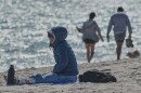 A bundled up Lucia Amato, of Argentina, sits on the shore while waiting for a friend in Miami Beach, Fla., Thursday, Jan. 29, 2026.A bundled up (AP Photo/Marta Lavandier)