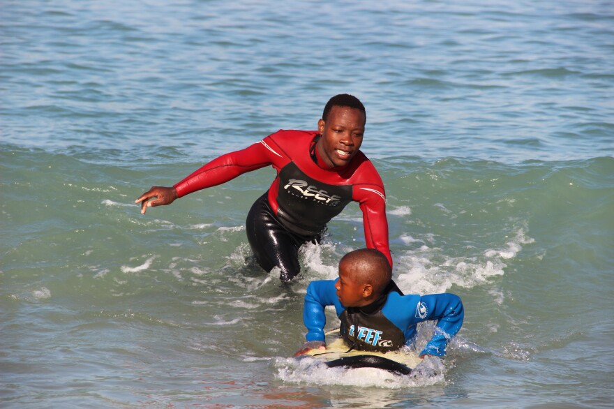 Lwandile Mntanywa helps a younger surfer learn to catch a wave. He's a "junior leader" in the Waves for Change program.