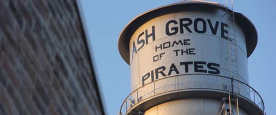 A water tower in the city of Ash Grove, displaying the name of the city and the name of the local school district's mascot.