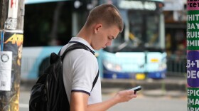 A kid uses his phone as he waits to cross the street.