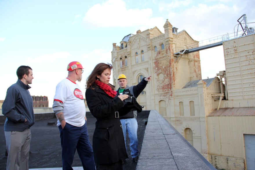 Genesee Beer Brand Manager Janine Schoos (foreground) checks a photo of the view from the future terrace of the Genesee Brew House. In the background is one of the buildings the brewery plans to demolish.