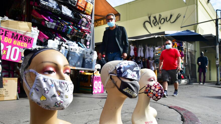 Pedestrians wearing facemasks walk past a display of mannequin heads also wearing facemasks earlier this month in Los Angeles.