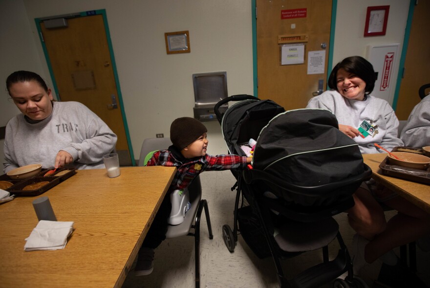 Kirshawn, 2, makes a new friend  with a newborn in a stroller next to him during the inmates' breakfast meal.