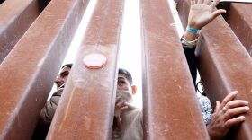 Immigrants seeking asylum in the U.S., who are stuck in a makeshift camp between border walls between the U.S. and Mexico, reach and look through the border wall as volunteers offer assistance on the other side in San Diego, California.