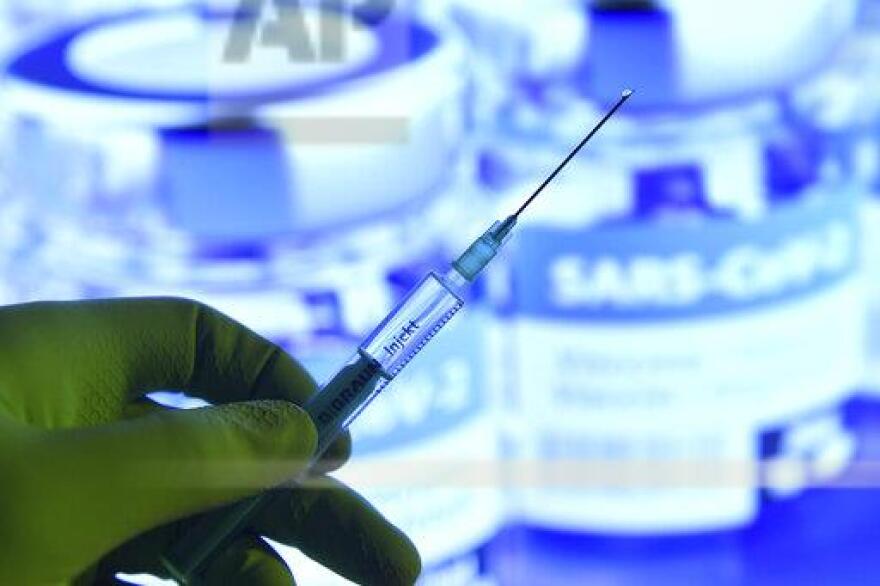 A hand wrapped in rubber gloves holds a disposable syringe of vaccine for injection in a needle. 