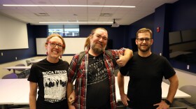 Woman stands next to two men in a classroom. 