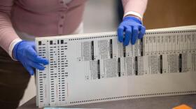 After running through a vote-counting machine, an election worker gathers ballots
