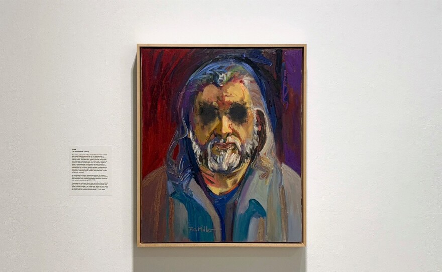 A painting of a man with grey hair and a grey beard hangs in a gold frame on the wall.