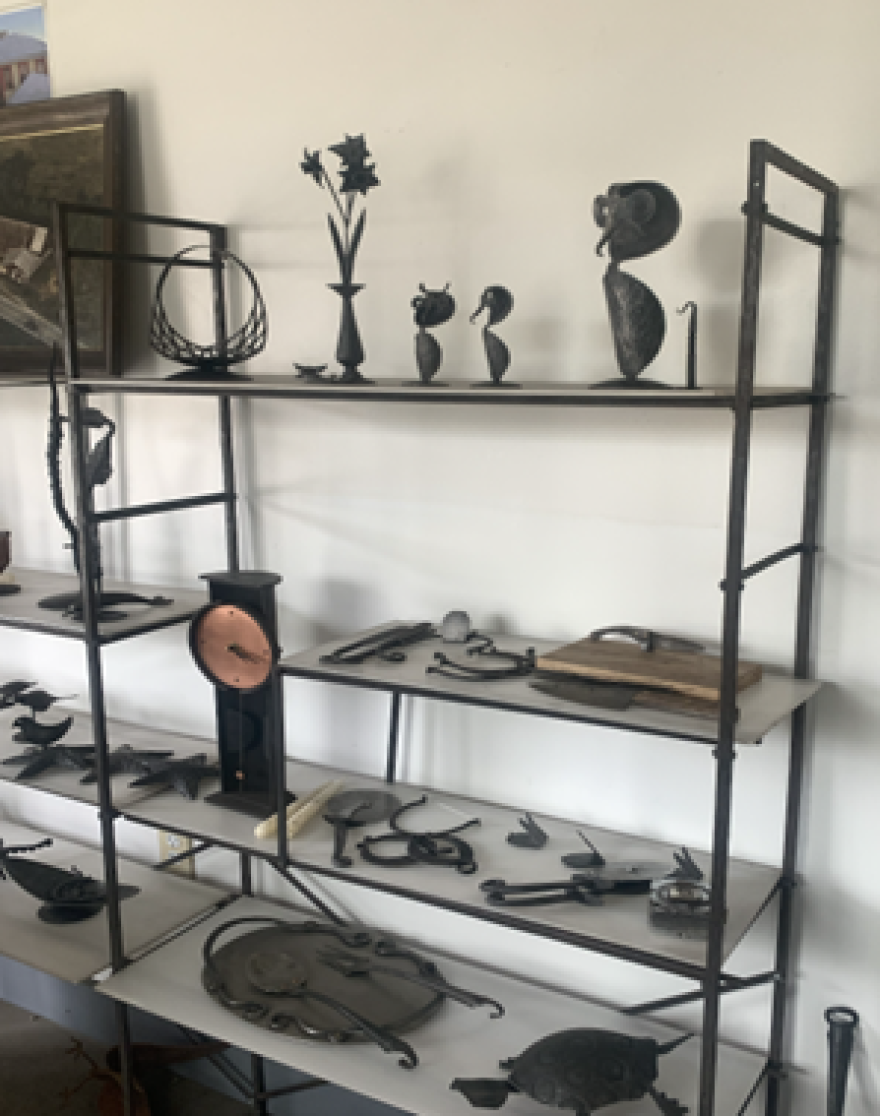 A black shelf against a white wall with metal sculptures on it. 