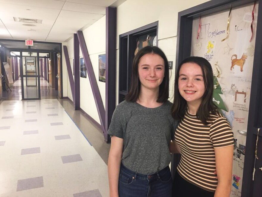 Two young people stand in a school hallway.