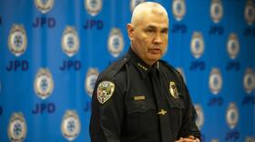 A white, white-haired man in a police uniform speaks at a lecctern in front of blue background