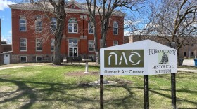 A sign in front of an old brick building surrounded by trees and green grass.