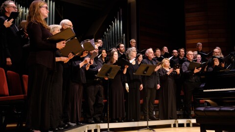 A group of vocalists stand on stage holding choirbooks.