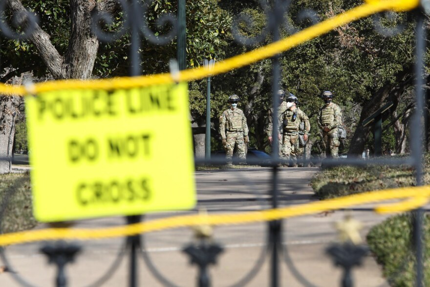 Law enforcement personnel can be seen behind the closed gate of the Texas Capitol grounds. A sign on the gate reads, "Police line do not cross. 