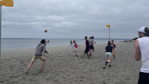People throw a ball up and run around on a beach on a cloudy day.