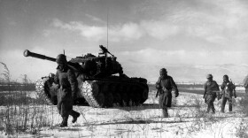 Four US soliders march through the snow next to a tank. 