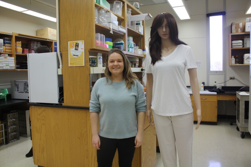 a petite white woman smiles and stands next to a mannequin dressed in white