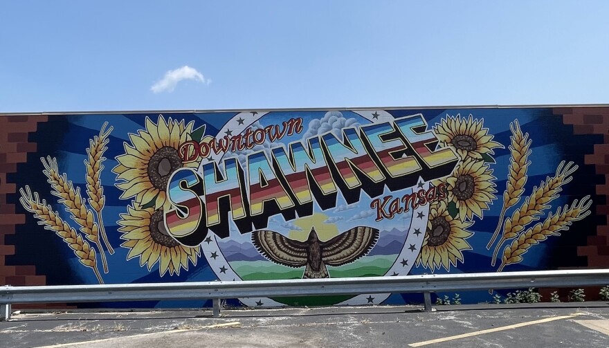 A brightly colored mural saying "Downtown Shawnee Kansas" with sunflowers, wheat, and a red tailed hawk.