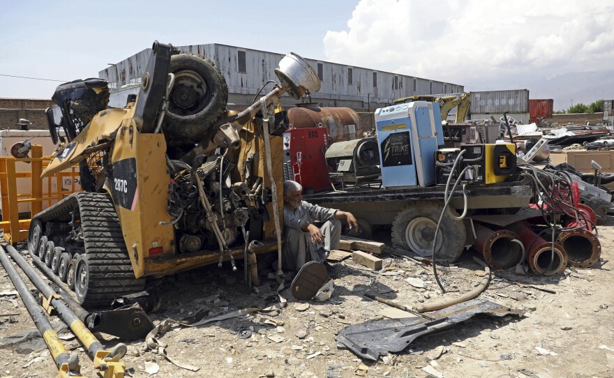 A man rests in the shade of destroyed machinery sold by the U.S. military to a scrapyard outside Bagram Air Base.