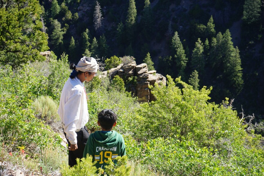 Apprentice weaver and potter Casey Teseny shows a youngster a yellow hand he painted on a rock face near the Kady family sheep camp in June 2026.