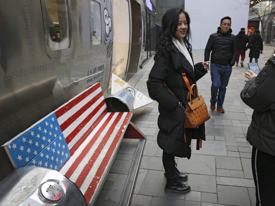 Chinese shoppers spend their time next to a bench painted with the U.S. flag at the capital city's popular shopping mall in Beijing. During trade talks this week, the two sides face potentially lengthy wrangling over technology and the future of their economic relationship.