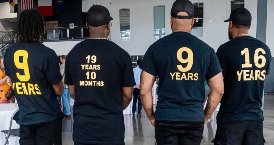 Members of the Organization of Exonerees wear t-shirts displaying the exact number of years they spent wrongfully incarcerated for crimes they did not commit. All the t-shirts are black and the numbers are on the back. The far left on says 9 years. The one next to it says 19 years and 10 months. The next one also says 9 years and the last says 16 years. 
