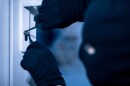 Closeup of gloved robber in a black mask cracking a door lock with metal picklock tool 