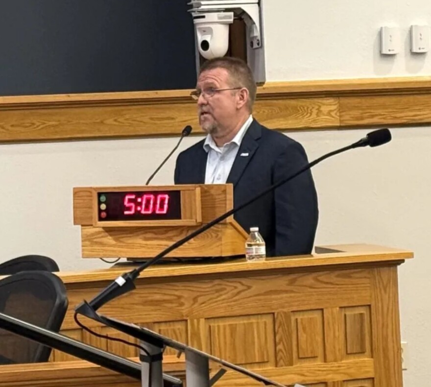 Man wearing suit jacket speaks behind podium at a meeting 