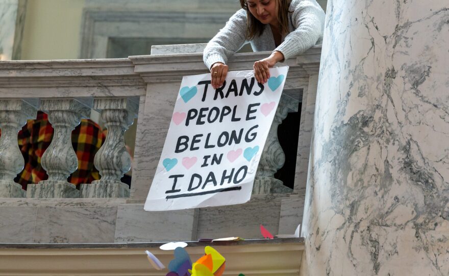 A woman uses a sign that says "Trans People belong in Idaho" to clear out paper hearts wedged on the side of the balcony overlooking the Capitol rotunda. 