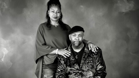 Renee Peoples stands with her hands resting on the shoulders of her seated husband, Bobby.