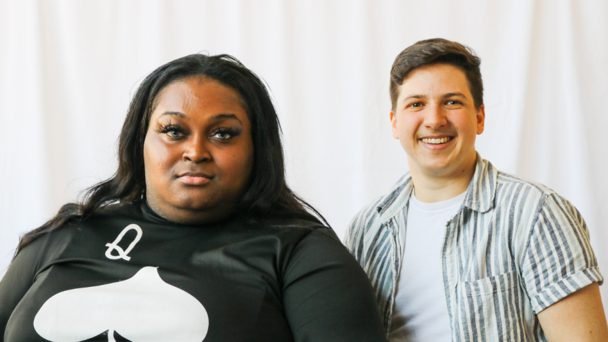 Two coworkers, a Black woman and White man, pose for a portrait in front of a white backdrop 