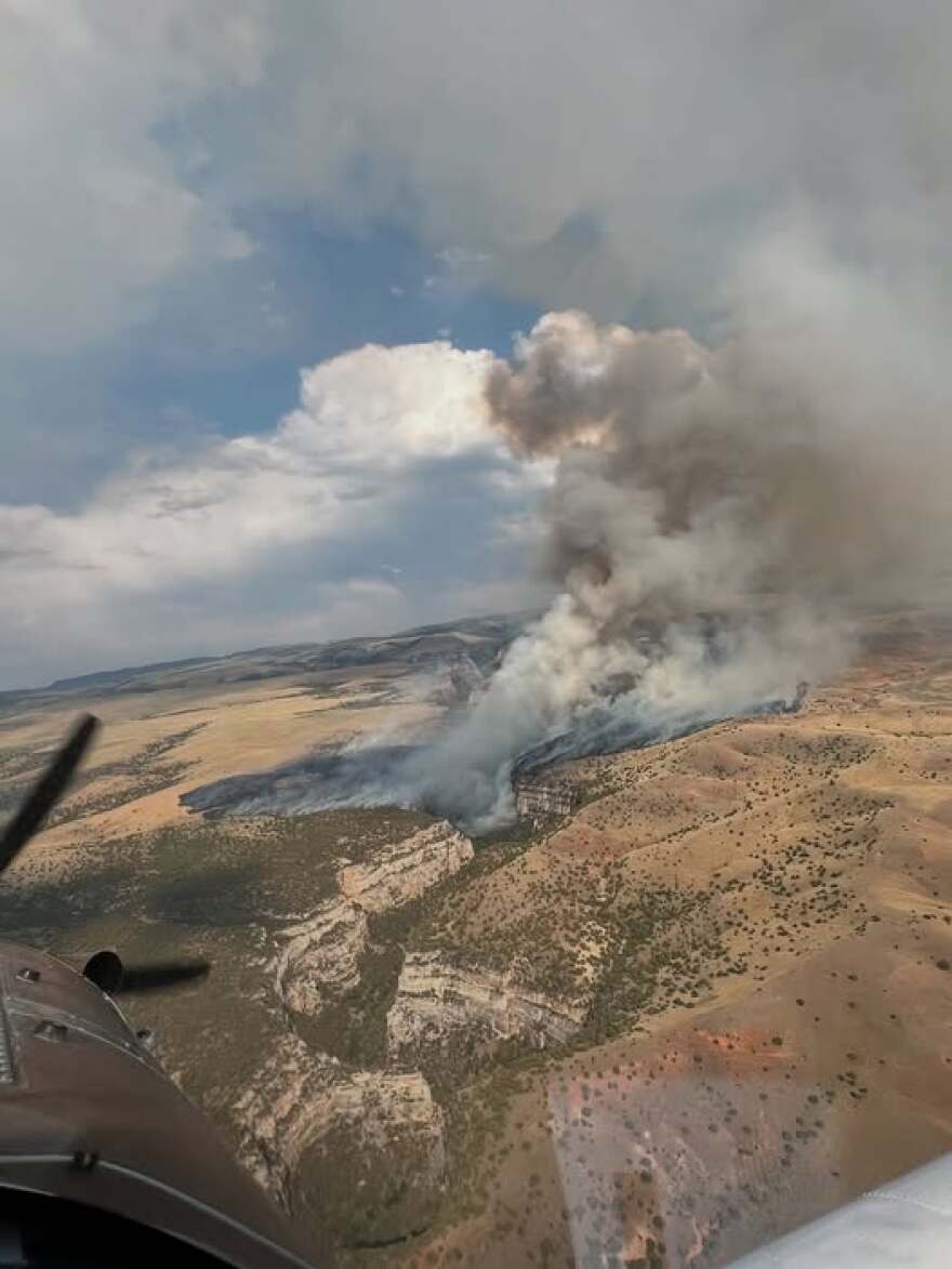 An aerial view of a deep canyon, with a fire burning on the left rim.