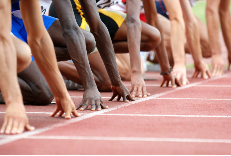 Five pair of hands are poised on the start line of a running track.
