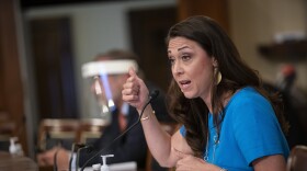 Rep. Jaime Herrera Beutler is sitting in front of a microphone wearing a blue shirt. She is holding her thumbs up.