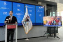 A man speaks at a podium beside an Illinois flag, with multiple screens behind him displaying “Every Student Initiative.” A monitor shows a group photo of children.