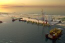 a mockup computer-generated graphic of an offshore wind terminal, with parts of floating offshore wind turbines, boats and cranes.