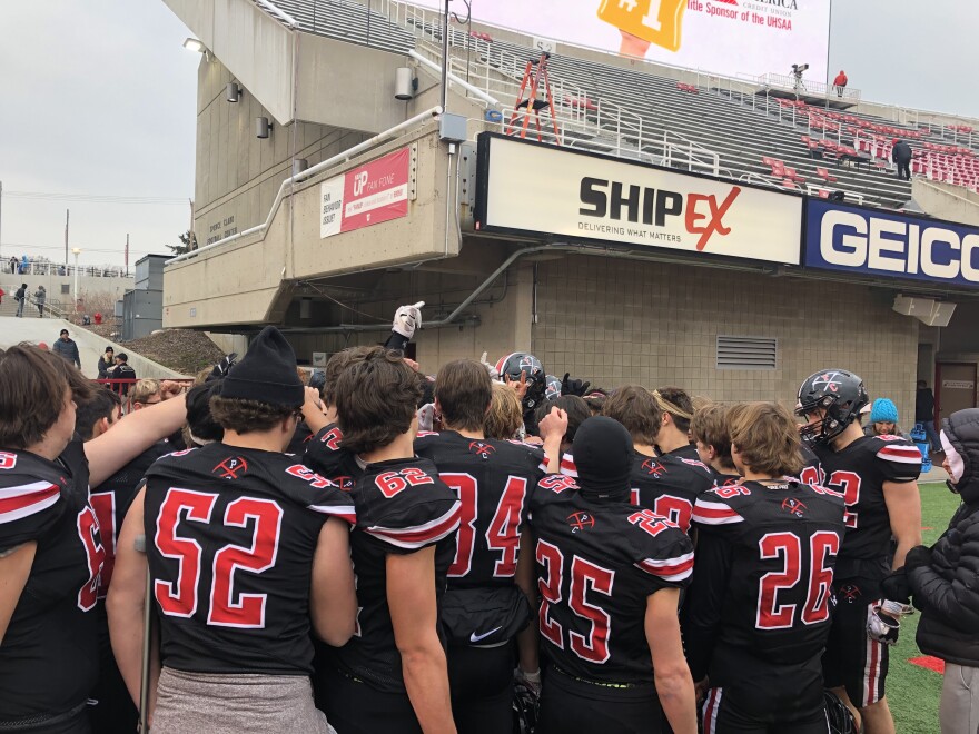 Football players gather in a circle to raise their arms and let out a unified cheer of "Family" at the end of their season