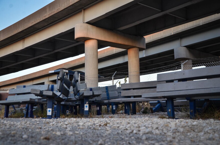 Grey benches are lined up in rows in a gravel lot