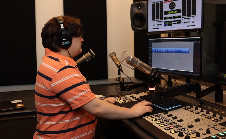 Charlie Smith, wearing headphones and standing in front of a microphone, mixing board and computer screen.