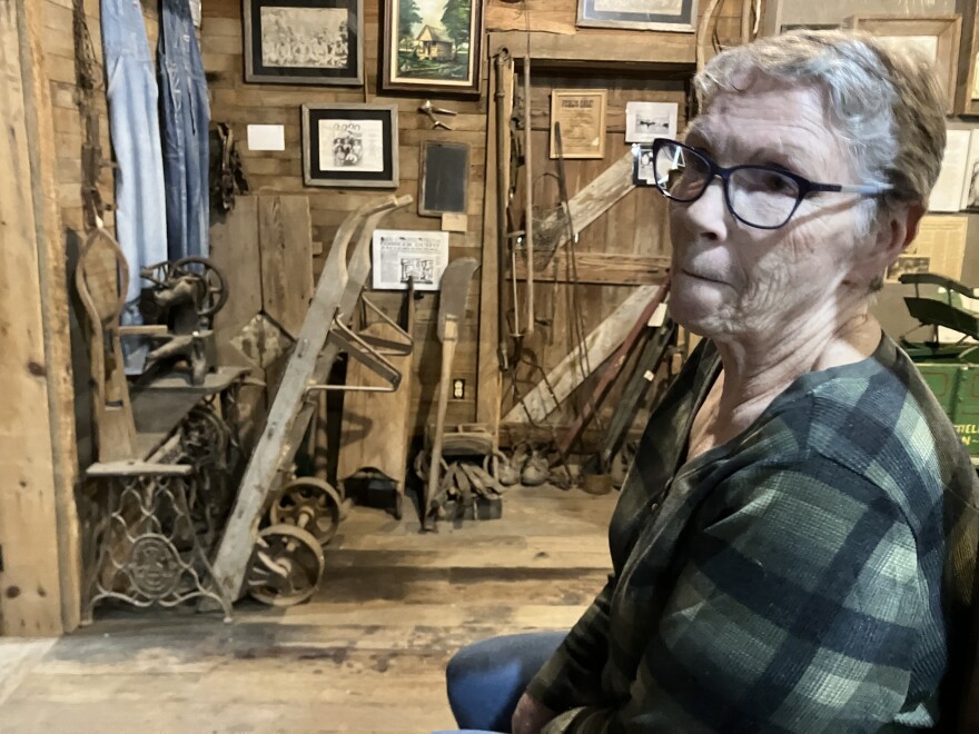 Betty Manning lived in Fair Grove roughly 50 years. She chats with an Ozarks Public Radio reporter, flanked by milling and farm tools gathered from nearby homesteads, on Sept. 12, 2024.