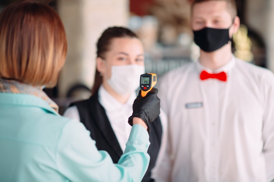 The Manager of a restaurant or hotel checks the body temperature of the staff with a thermal imaging device