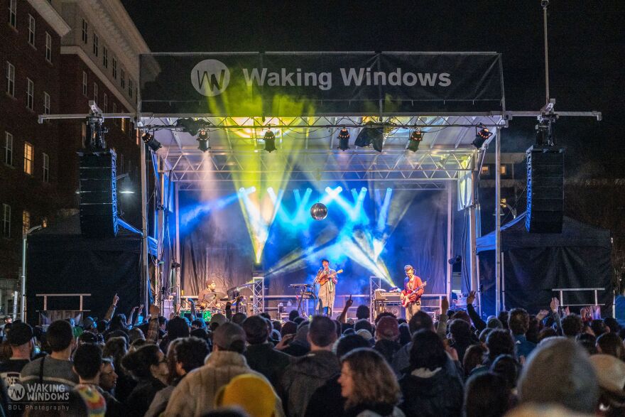 An outdoor performance stage, with lights and performers and a crowd gathered in front.