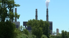 A coal plant on a sunny day, with a large tree and an open field in the foreground.