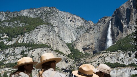 Park rangers meet in front of Yosemite Falls in 2016 in Yosemite National Park in California. Increased fees are expected to boost funding for park maintenance across the country.