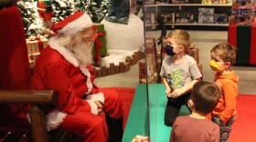 A man dressed like santa sits behind a plexiglass barrier