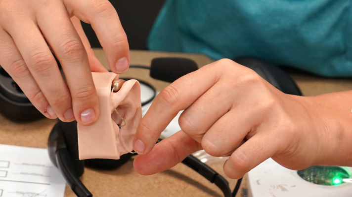 A health care professional demonstrates a hearing aid at a previous M