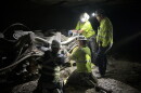 Four men in safety shirts work on a machine in the dark, illuminated with headlamps. 