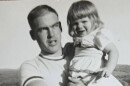 Black and white photo of smiling young girl in a white dress, held by young man looking pensive