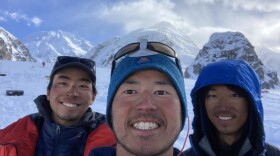 three men pose for a selfie in front of snow mountains