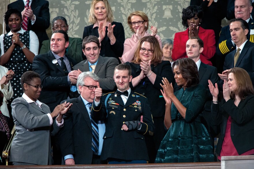 First Lady Michelle Obama, Dr. Jill Biden, and First Lady's box guests acknowledge Army Ranger Cory Remsburg, who was recognized by President Barack Obama in the State of the Union address in the House Chamber at the U.S. Capitol in Washington, D.C., Jan. 28, 2014.  (Courtesy of Little, Brown and Company/Pete Souza)